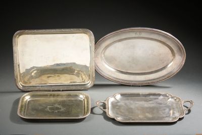 trois plateaux en argent et un plateau en argent muni de poignées, posés sur une table