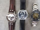 three watches sitting on a table with a brown leather strap