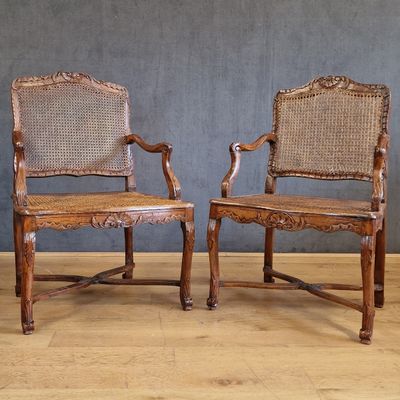 two wooden chairs with wicker back and arms against a gray wall