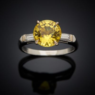 a close up of a yellow sapphire and diamond ring on a black surface