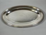an oval silver plate with a beaded edge sits on a table