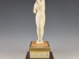 une statue blanche représentant une femme tenant une balle, posée sur un socle en marbre