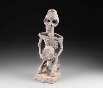 une statue représentant un squelette tenant un bol posé sur une table