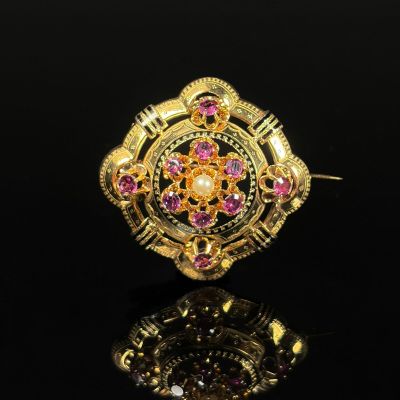 a close up of a gold and pink stone broochle on a black surface