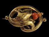 une image représentant une broche en or ornée de perles de corail sur fond noir
