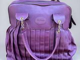 le sac à main violet est posé sur une surface blanche, avec un fond gris