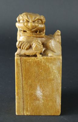 une figurine ancienne sculptée représentant un chien, posée sur un socle