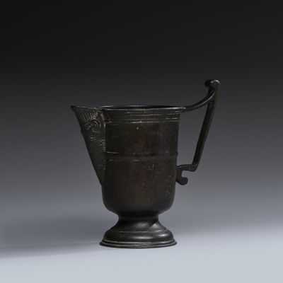 une vieille tasse en métal noir avec une anse, posée sur un socle