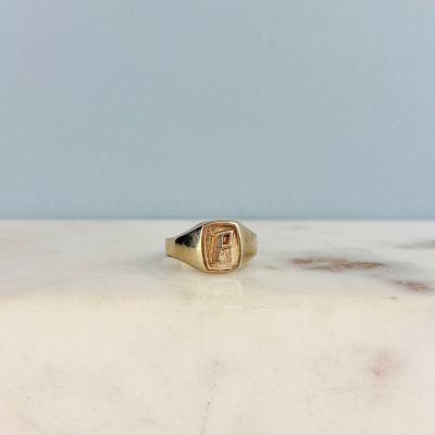 a close up of a gold signet ring on a marble surface