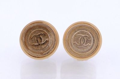 deux paires de boucles d'oreilles Chanel dorées posées sur une surface blanche