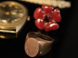 a gold watch, a ring, and a red flower on a black surface