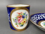 a blue cup with a gold rim next to a bowl with flowers