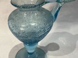 un pichet en verre bleu muni d'une anse, posé sur une table blanche