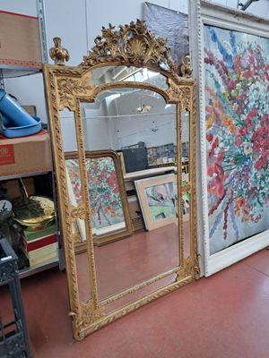 un grand miroir au milieu d'une pièce où est accroché un tableau au mur