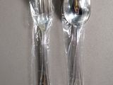 two forks and spoons wrapped in plastic on a table