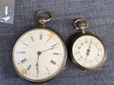 two antique pocket watches sitting next to each other on a blue cloth
