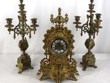 trois bougeoirs en laiton et une horloge posés sur une table