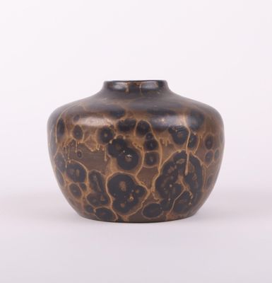 un vase marron parsemé de taches noires sur un fond blanc