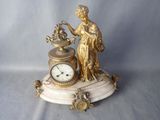 une statue en or représentant une femme tenant une horloge, posée sur un socle en marbre