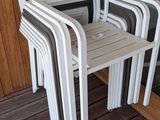 plusieurs chaises en plastique blanc posées sur une terrasse en bois, près d'une porte vitrée