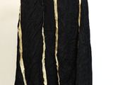 Quelqu'un tient une veste noire ornée de franges dorées, suspendue à un cintre.