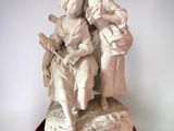 statue of a woman sitting on a man ' s lap on a red stand