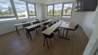 des tables et des chaises dans une pièce où est accrochée une télévision à écran plat au mur