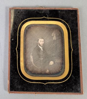 une vieille photo d'un homme en costume, assis sur une chaise