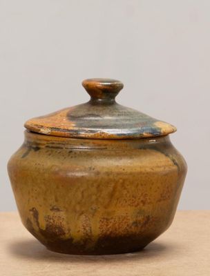 un petit pot marron muni d'un couvercle, posé sur une table