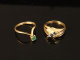 two gold rings with emerald stones on a black surface