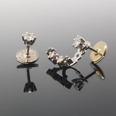 two pairs of diamond stud earrings sitting on top of a black surface