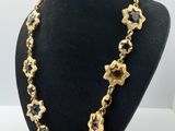 Le collier est en métal doré et présente un motif floral.