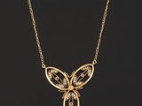 a gold butterfly necklace with diamonds on a black background
