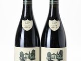 two bottles of red wine sitting next to each other on a white surface