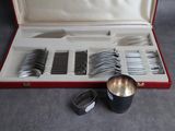 des couverts dans un coffret rouge posé sur une surface grise, comprenant une cuillère en argent et une tasse en argent