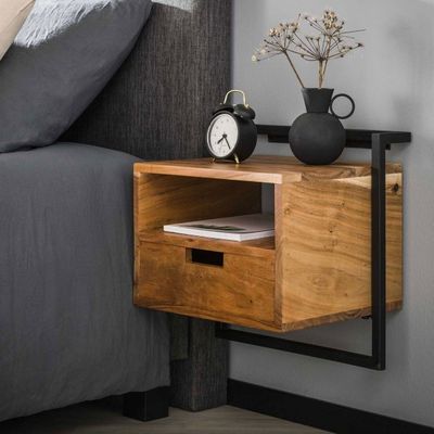 une petite table en bois sur laquelle se trouve une horloge, à côté d'un lit