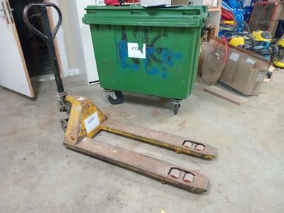 une poubelle verte posée sur une palette dans un garage