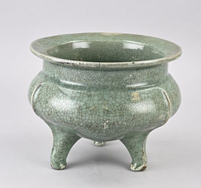 un petit pot vert à pieds posé sur une surface blanche