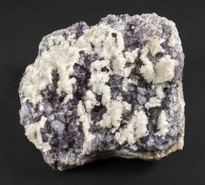 un gros plan sur un morceau de roche présentant des cristaux blancs et violets sur fond noir
