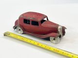 une petite voiture rouge à côté d'une règle, posée sur une surface blanche