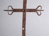 une croix en métal posée sur un socle en bois, sur fond blanc