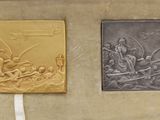 two gold and silver plaques on display in a case