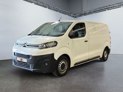 La camionnette blanche est garée dans une grande pièce au sol gris.