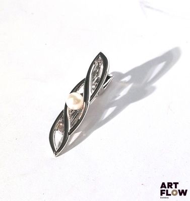 une broche en argent sertie d'une perle, posée sur un fond blanc