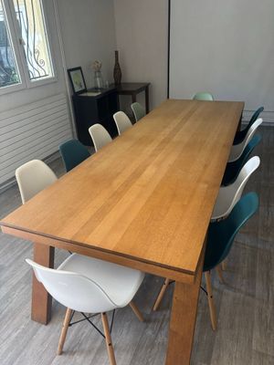 une grande table en bois avec des chaises blanches et un tableau accroché au mur
