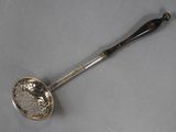 an antique silver spoon with a handle on a gray surface