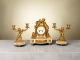 une horloge en or posée sur une table, à côté de trois bougies