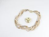 bracelet de perles orné d'un pendentif en forme de cœur doré sur fond blanc