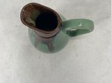 a small green vase with a brown handle on a white surface