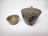 une vieille tasse et une soucoupe en laiton posées sur une surface blanche
